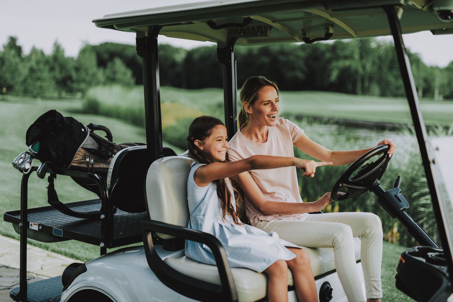 A parent and child driving a golf cart together, steering wheel in view